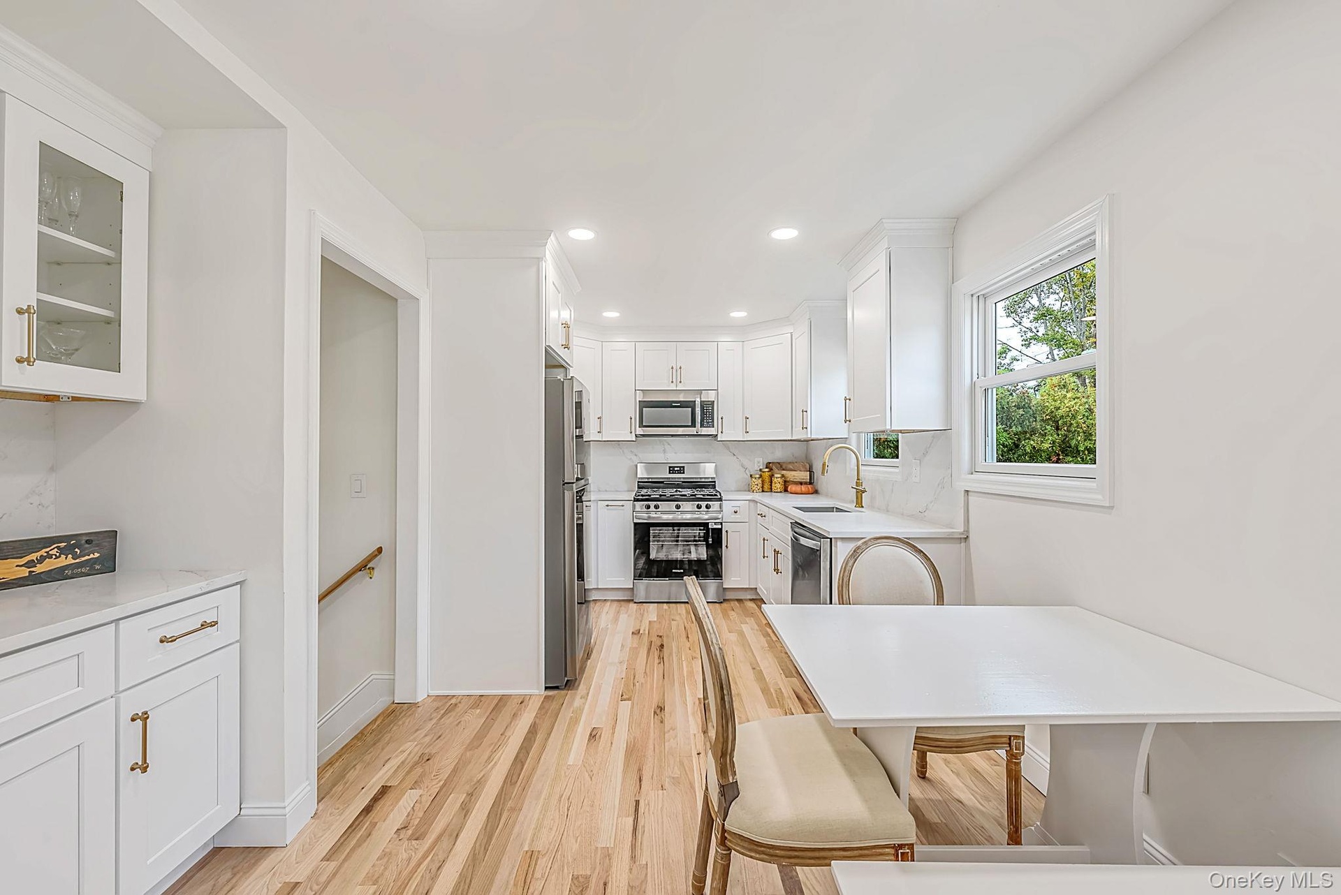 Kitchen featuring white shaker-style cabinetry, wood-finish flooring, stainless steel appliances, stone-look countertops, and recessed lighting