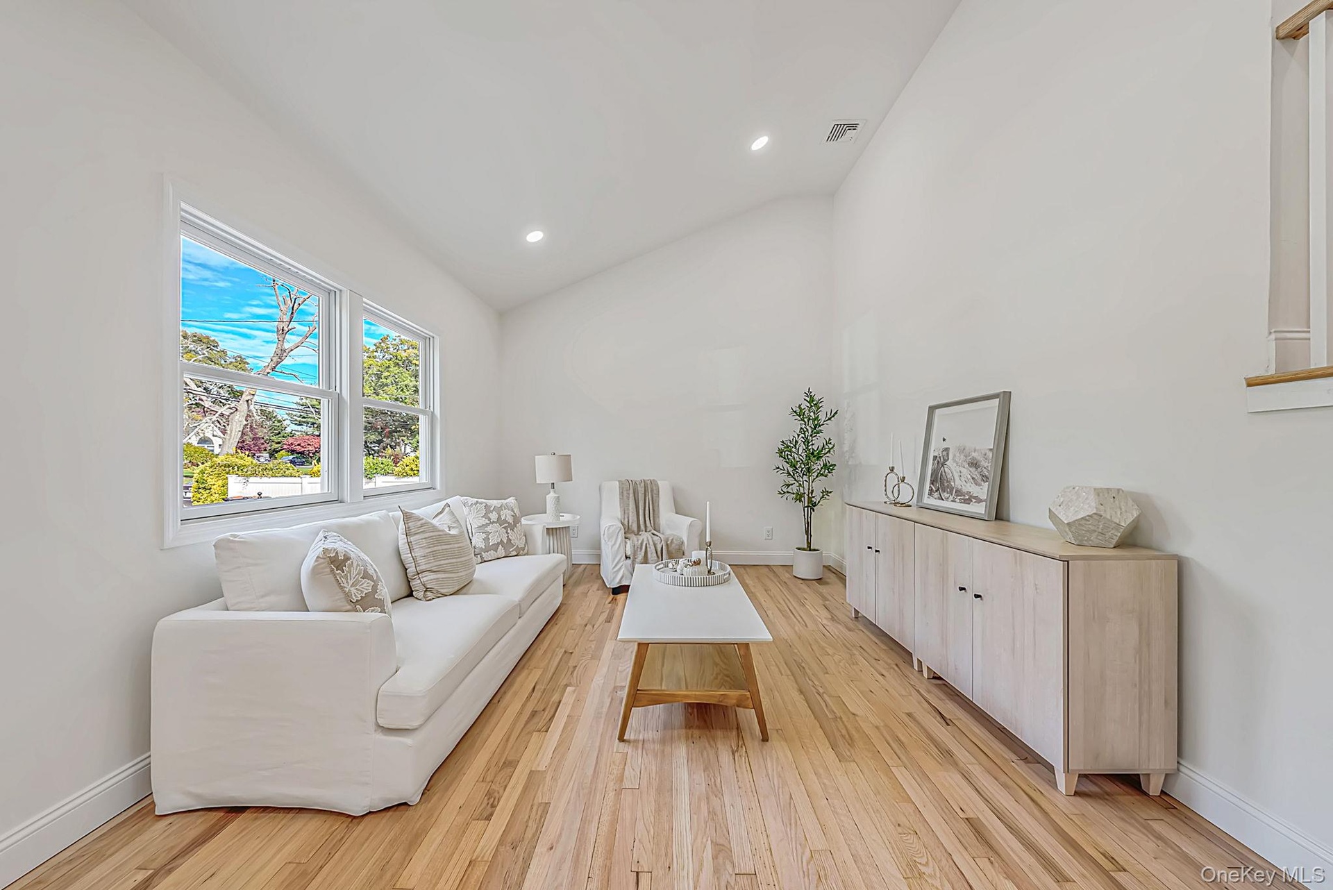 Living room with vaulted ceilings, wood-finish flooring, recessed lighting, and large windows