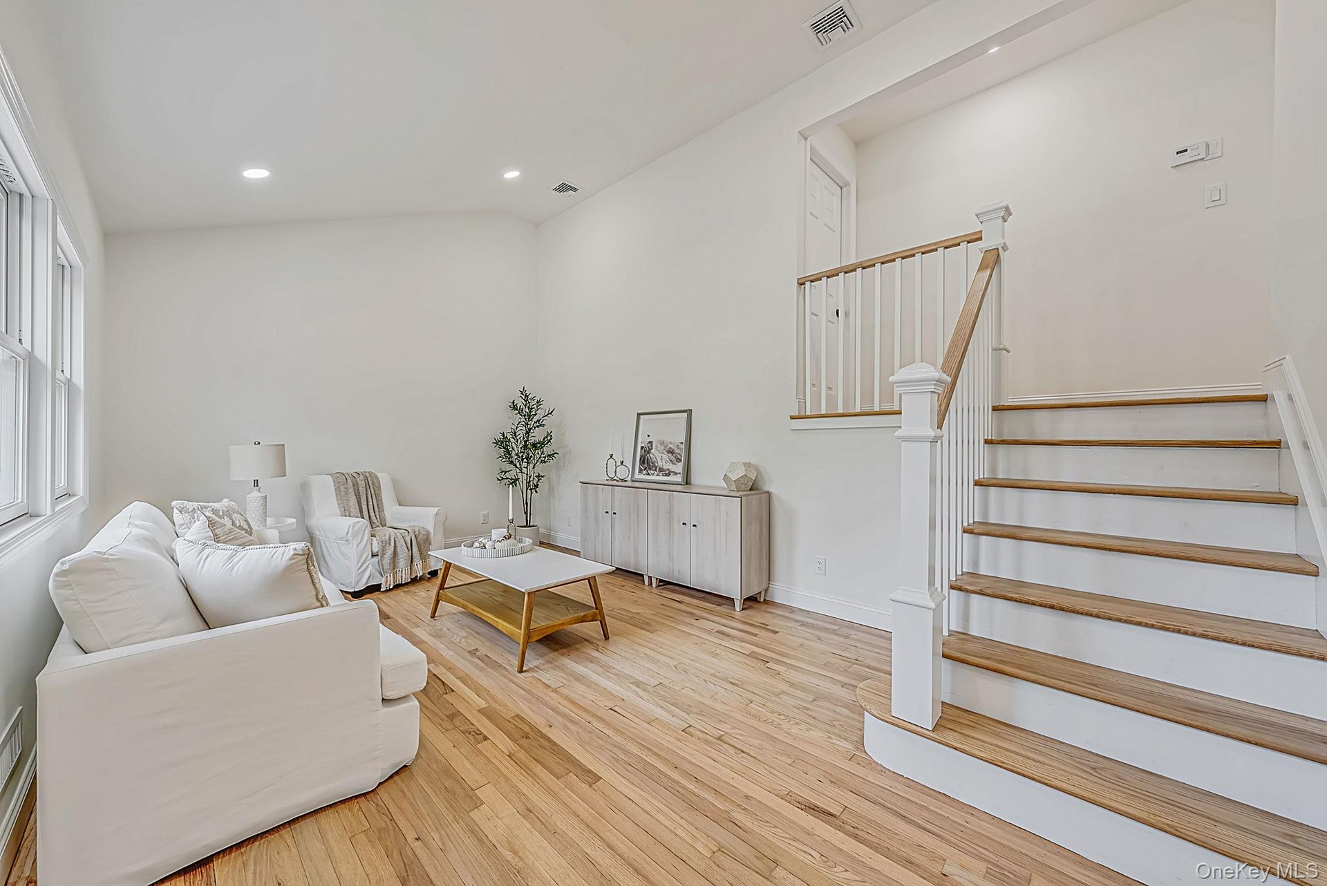 Living room with vaulted ceilings, wood-finish flooring, recessed lighting, and a staircase featuring white balusters with wood-finish treads