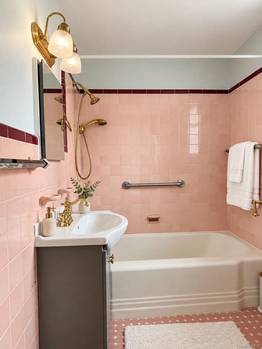 Bathroom featuring ceramic wall tiling with burgundy accent trim, a white porcelain pedestal sink with a brass-finish faucet, a brass-finish handheld 