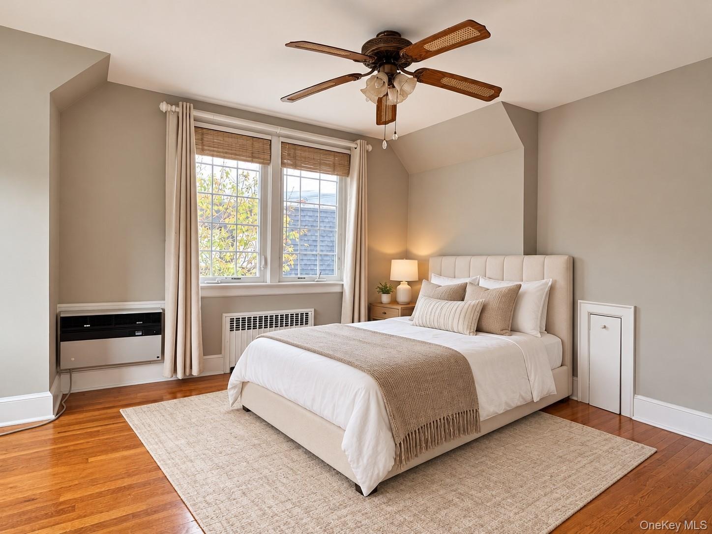 Hardwood flooring, multi-pane windows with integrated wooden blinds, a ceiling fan with integrated lighting, and a wall-mounted climate control unit