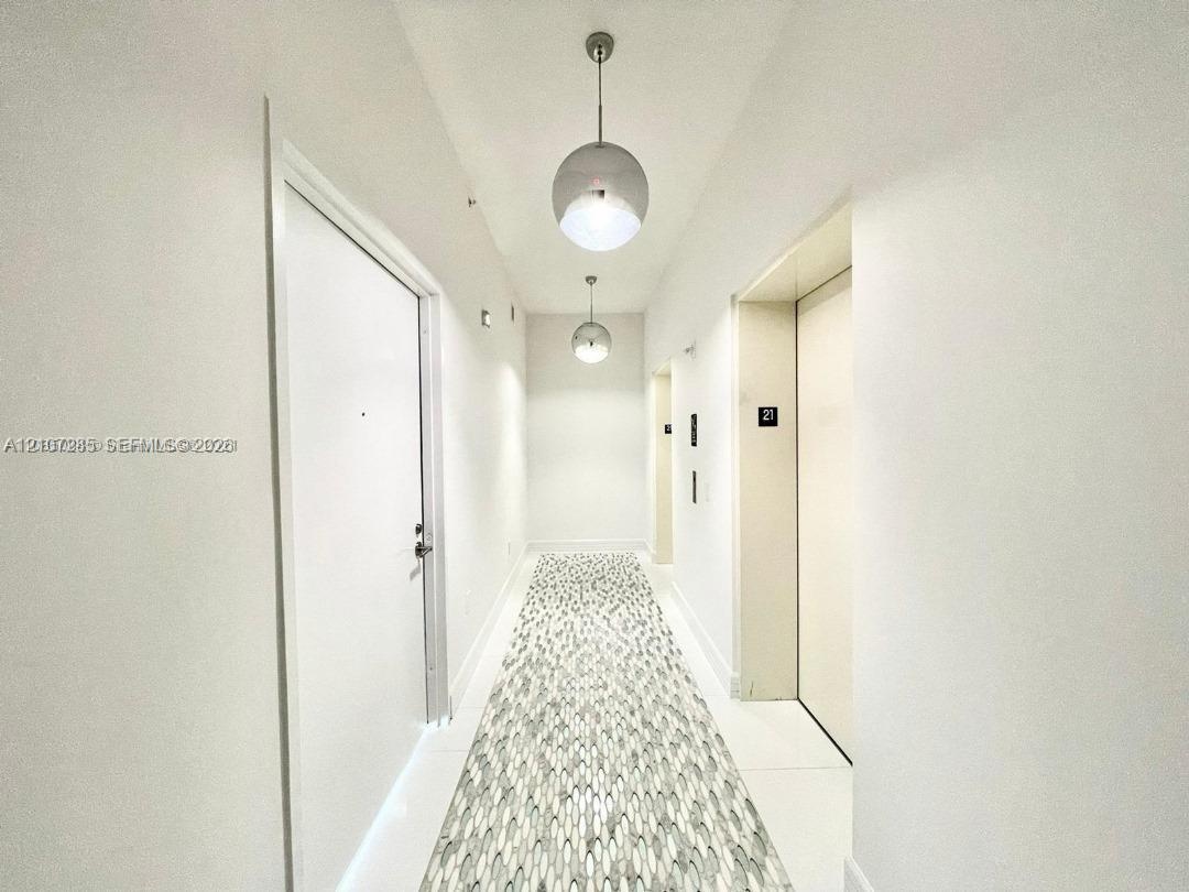Hallway featuring crisp white walls, large-format tile flooring with a patterned mosaic inlay, and dual spherical pendant lighting fixtures