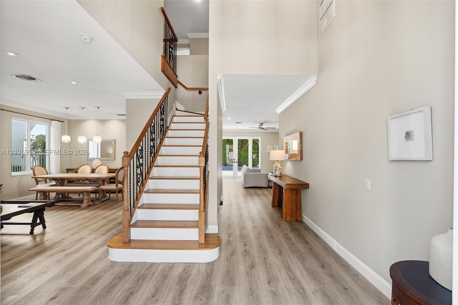Open-concept interior featuring wood-finish flooring, a grand staircase with decorative metal balusters and wood handrails, high ceilings, recessed li