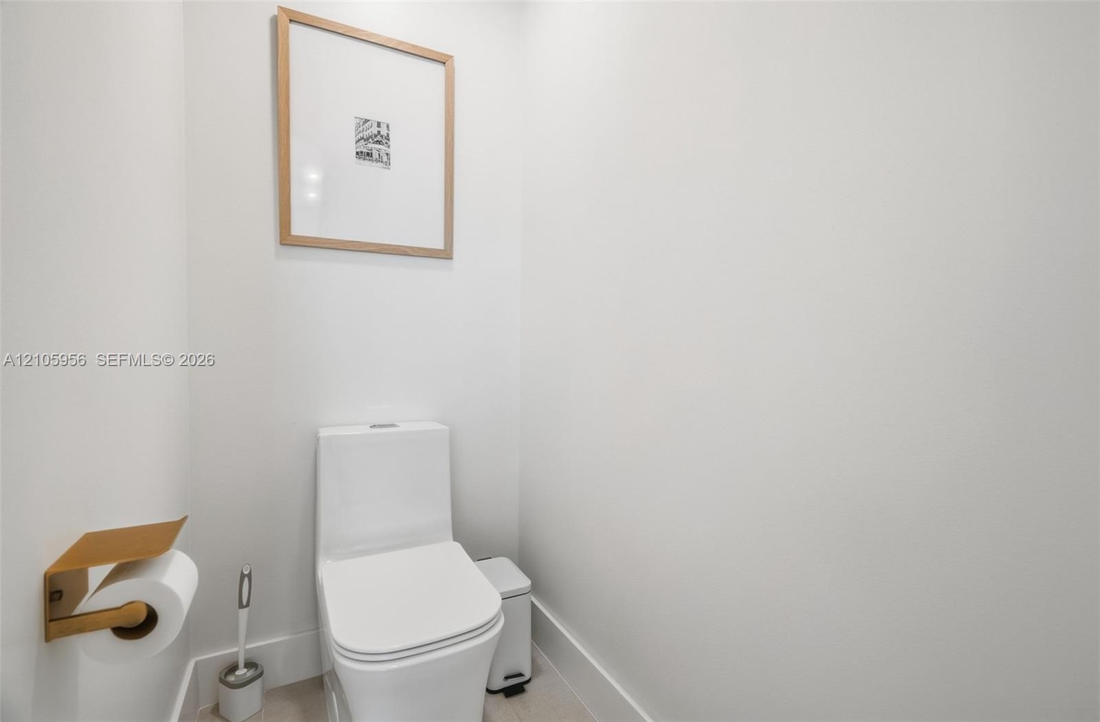 Minimalist powder room featuring a white dual-flush elongated toilet and a wall-mounted metallic gold finish toilet paper holder