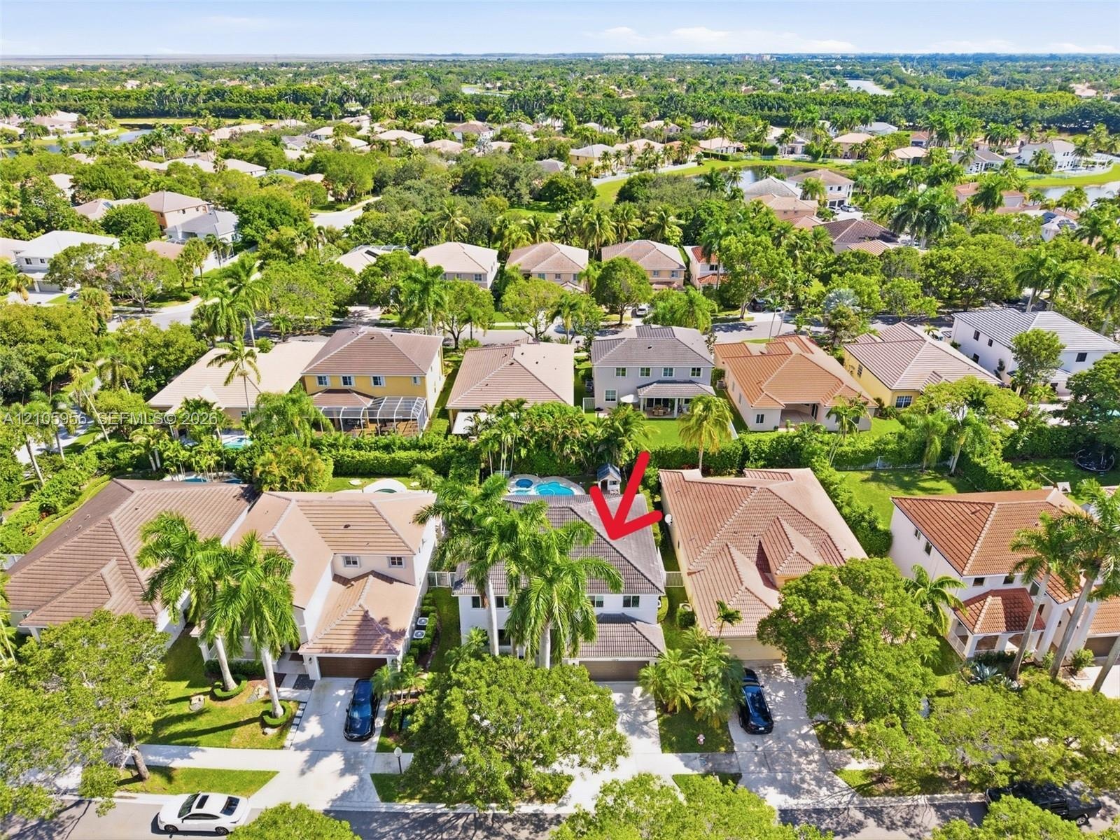 Aerial perspective featuring a two-story residence with a concrete tile roof, integrated swimming pool, attached multi-car garage, and mature palm tre