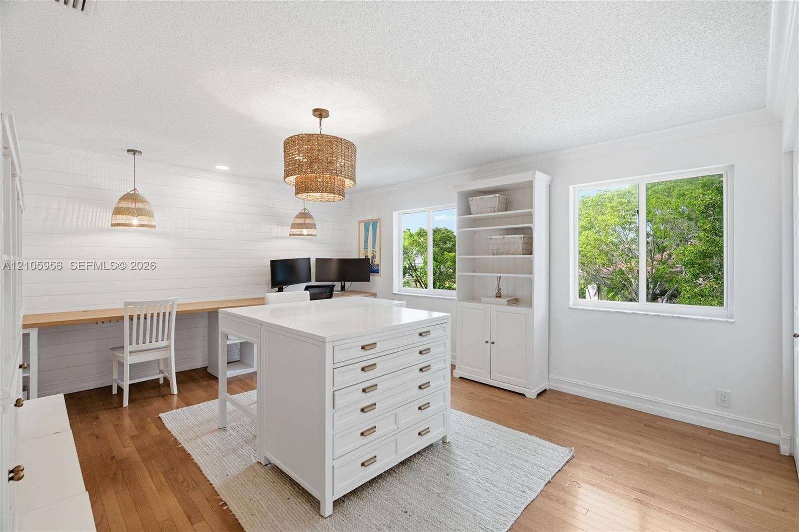 Room featuring white shiplap walls, built-in wooden desk, wood-finish flooring, white custom cabinetry with drawers, and multi-tiered pendant lighting