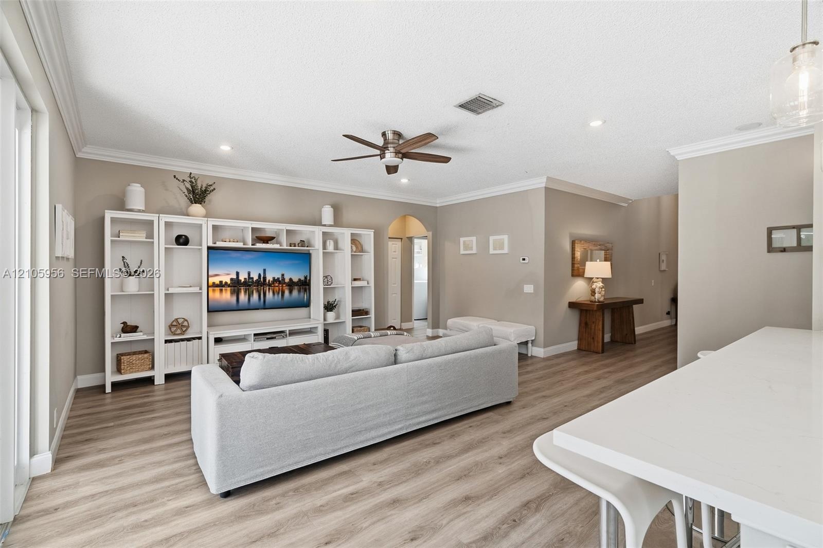 Living area featuring wood-finish flooring, white built-in cabinetry, crown molding, a ceiling fan, and recessed lighting