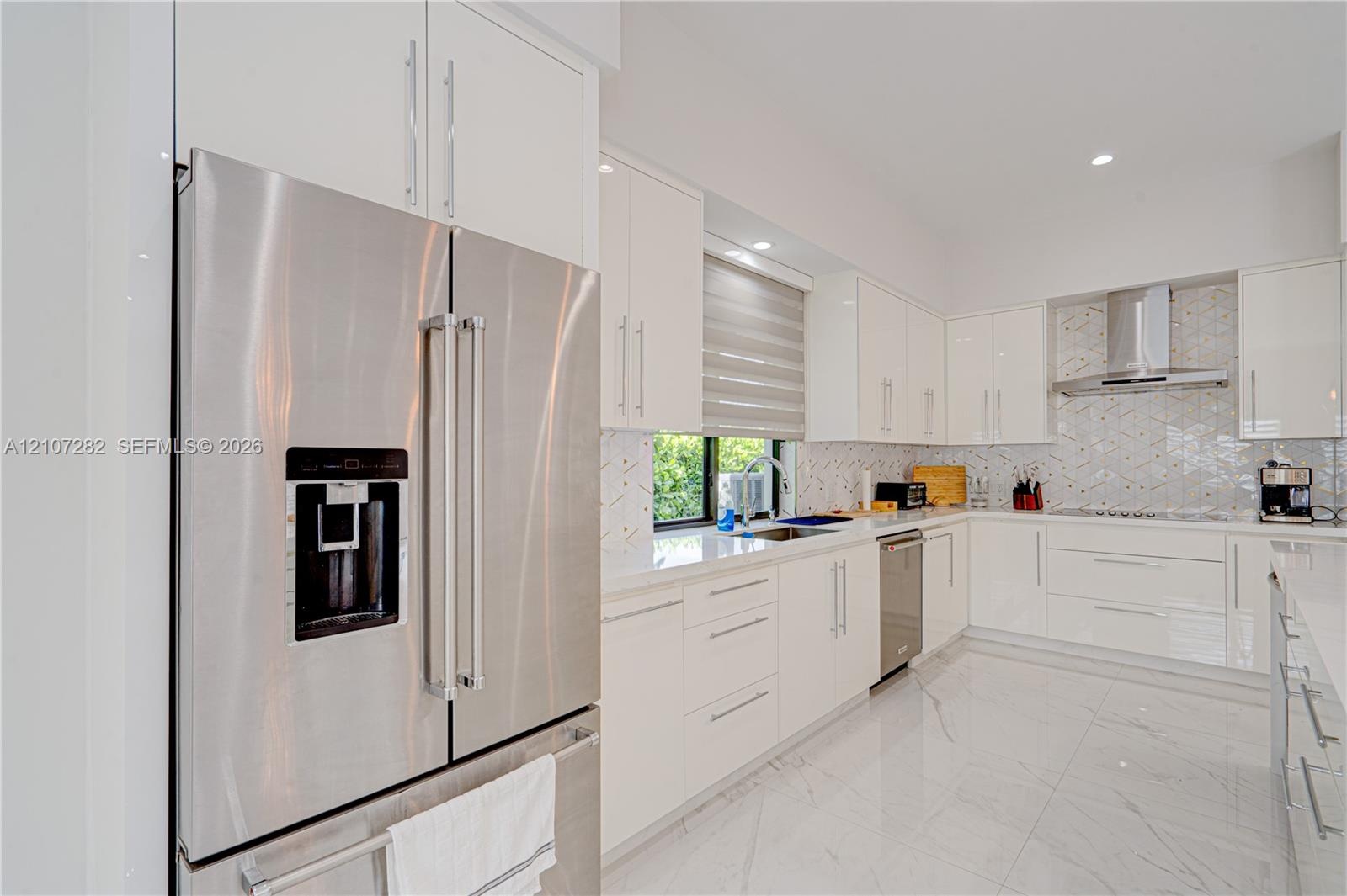 Kitchen featuring high-gloss white cabinetry, quartz countertops, stainless steel appliances, herringbone tile backsplash, and polished porcelain floo