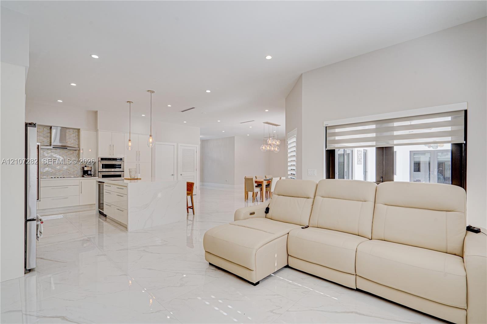 Open concept interior featuring high-gloss large-format tile flooring, stone-finish kitchen island, recessed lighting, and stainless steel built-in ap