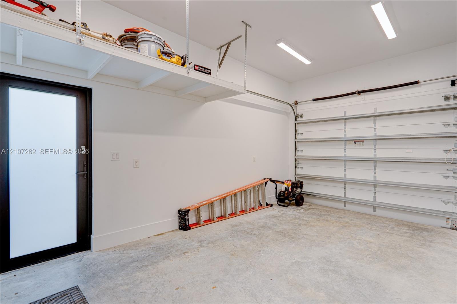 Finished garage featuring high-ceiling overhead storage shelving, linear LED lighting, and an exterior door with frosted glass paneling