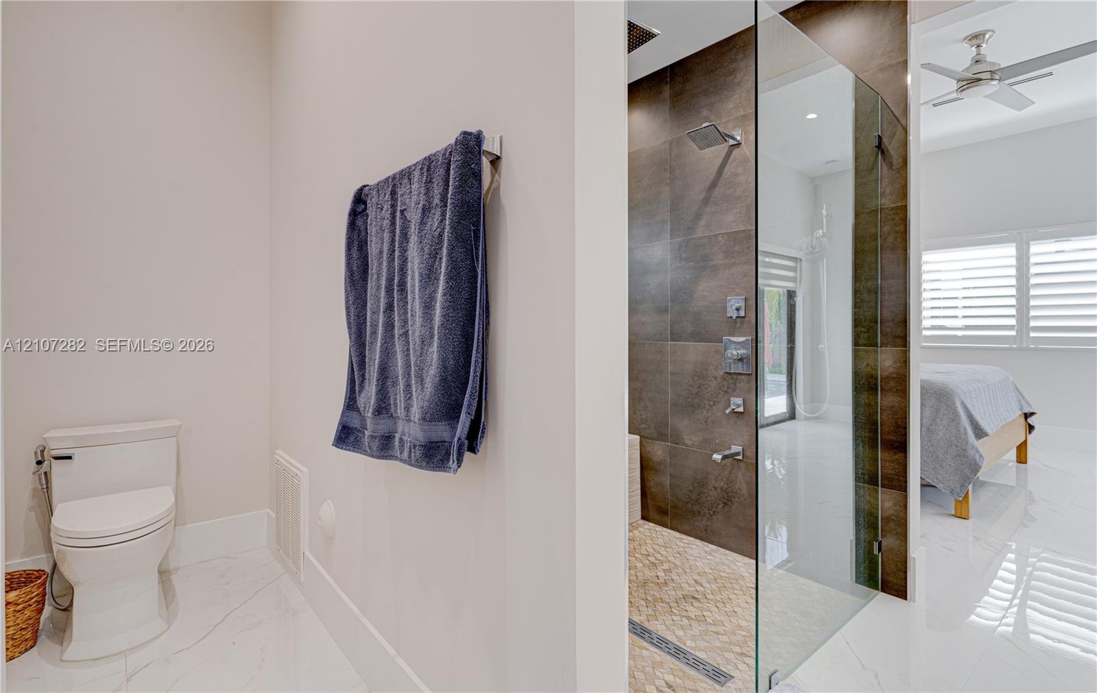 Walk-in shower with dark large-format tile surround, rainfall showerhead, and glass enclosure, complemented by porcelain flooring and a wall-mounted t