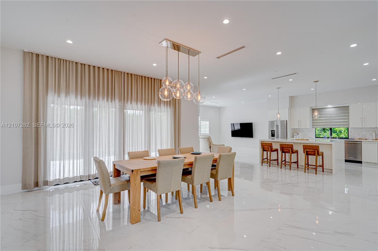 Open-concept interior featuring large-format polished stone flooring, recessed ceiling lighting, a multi-globe linear chandelier, and a kitchen island