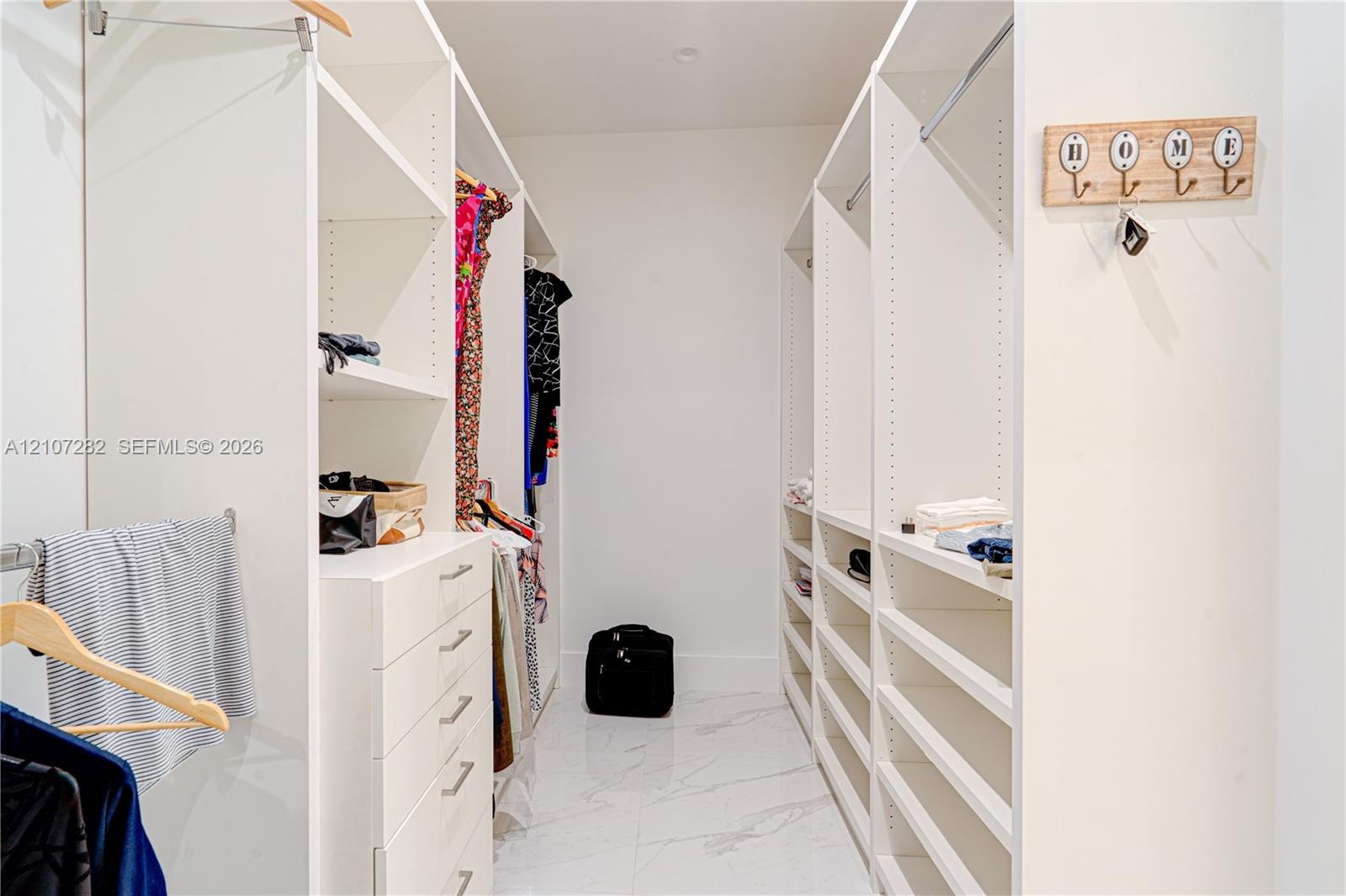 Walk-in closet featuring white built-in shelving, integrated dresser drawers, dual hanging rods, and large-format white tile flooring