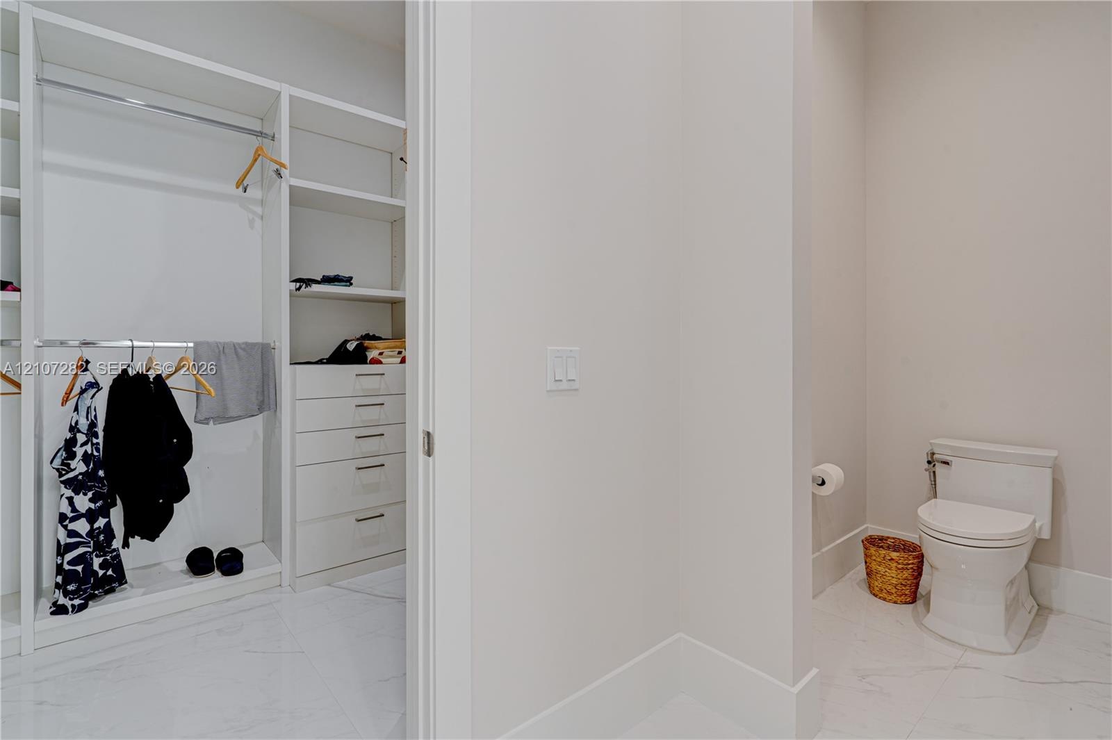 Custom walk-in closet featuring white built-in shelving and integrated drawer storage, paired with an enclosed water closet finished with stone-tile f
