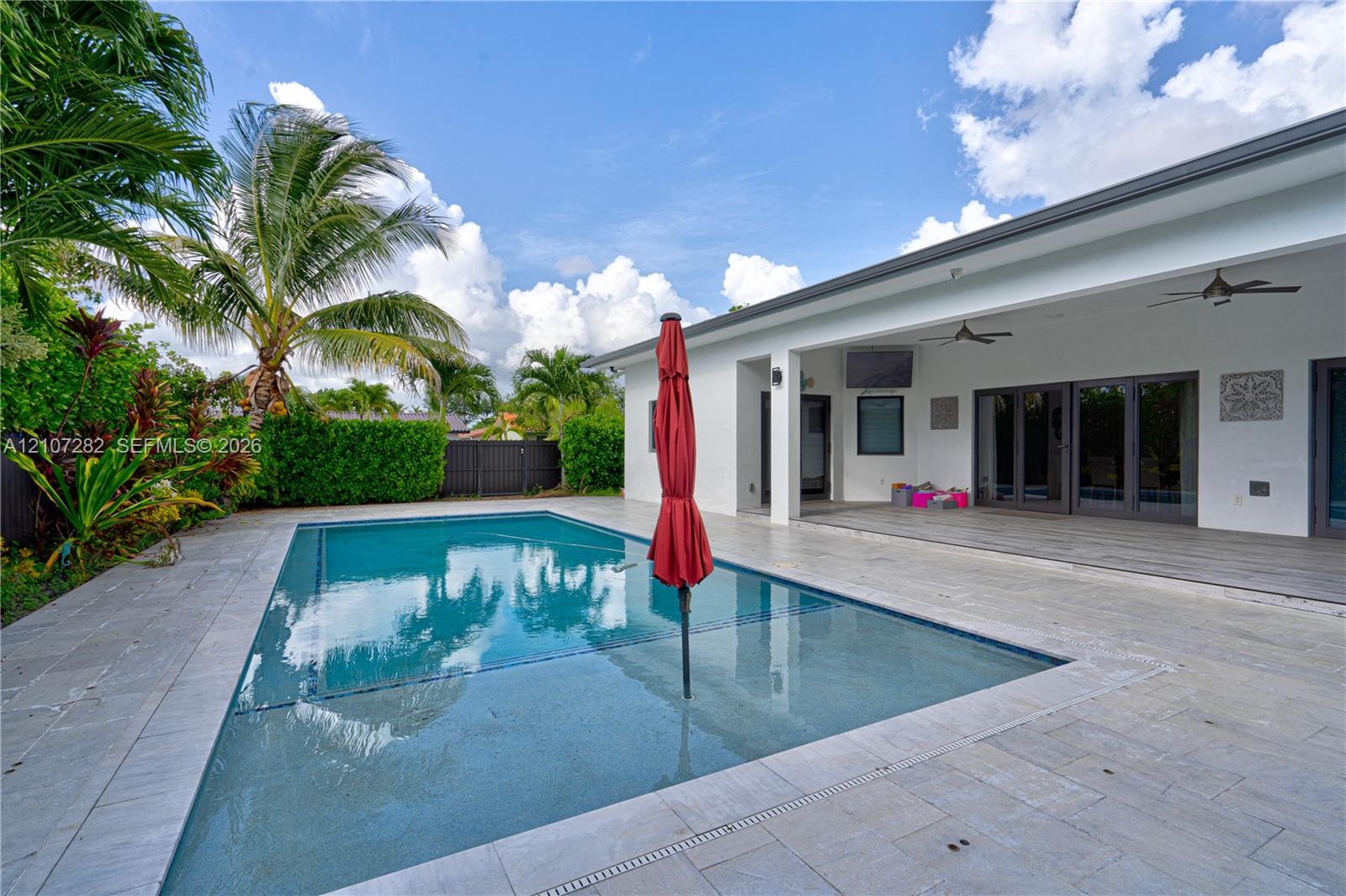 Outdoor patio featuring a covered lanai with ceiling fans, an integrated rectangular swimming pool, and stone-finish paving