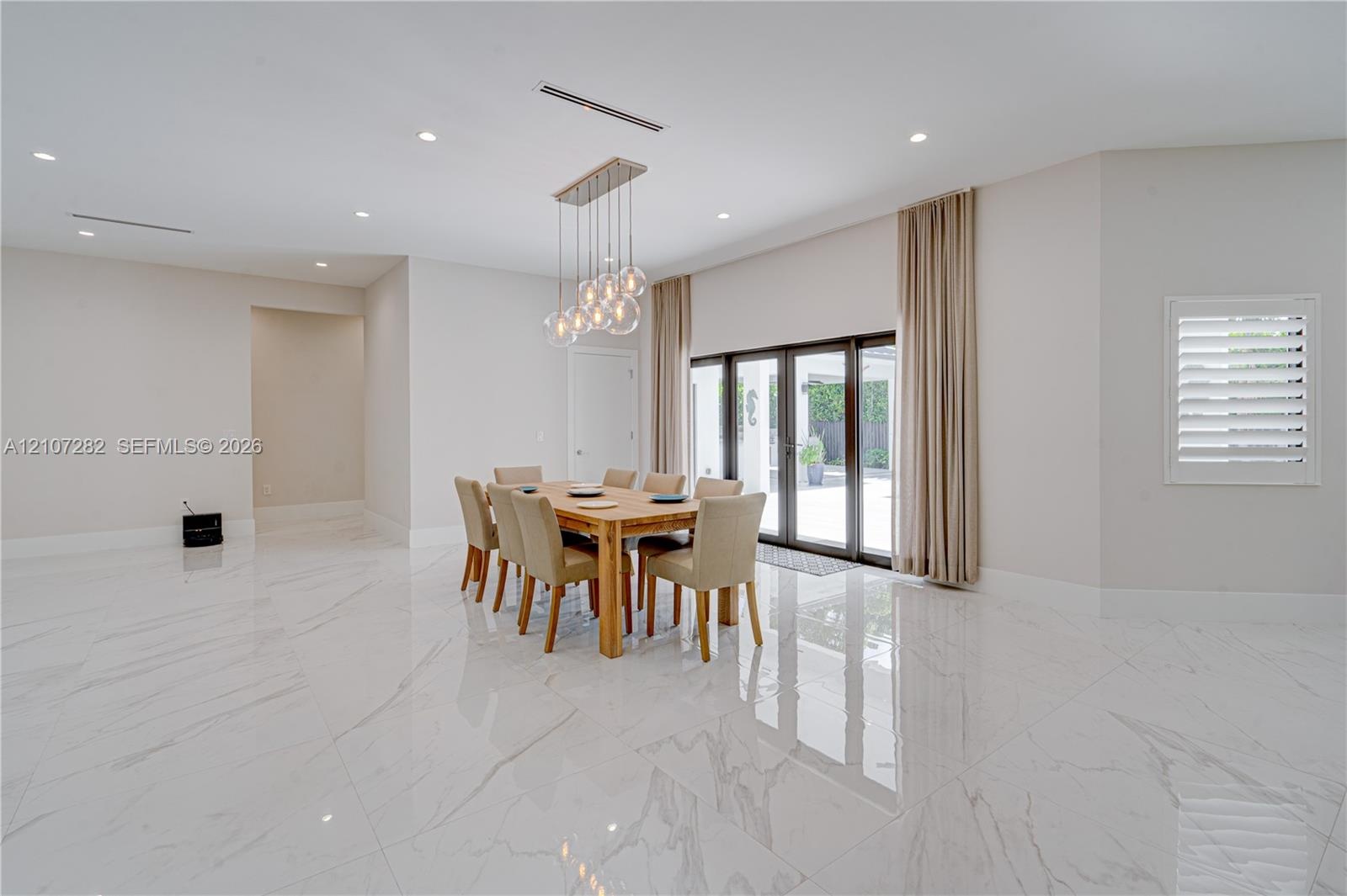 Large-format, polished stone flooring featuring distinct veining, multi-pendant glass orb chandelier, recessed ceiling lighting, and floor-to-ceiling 