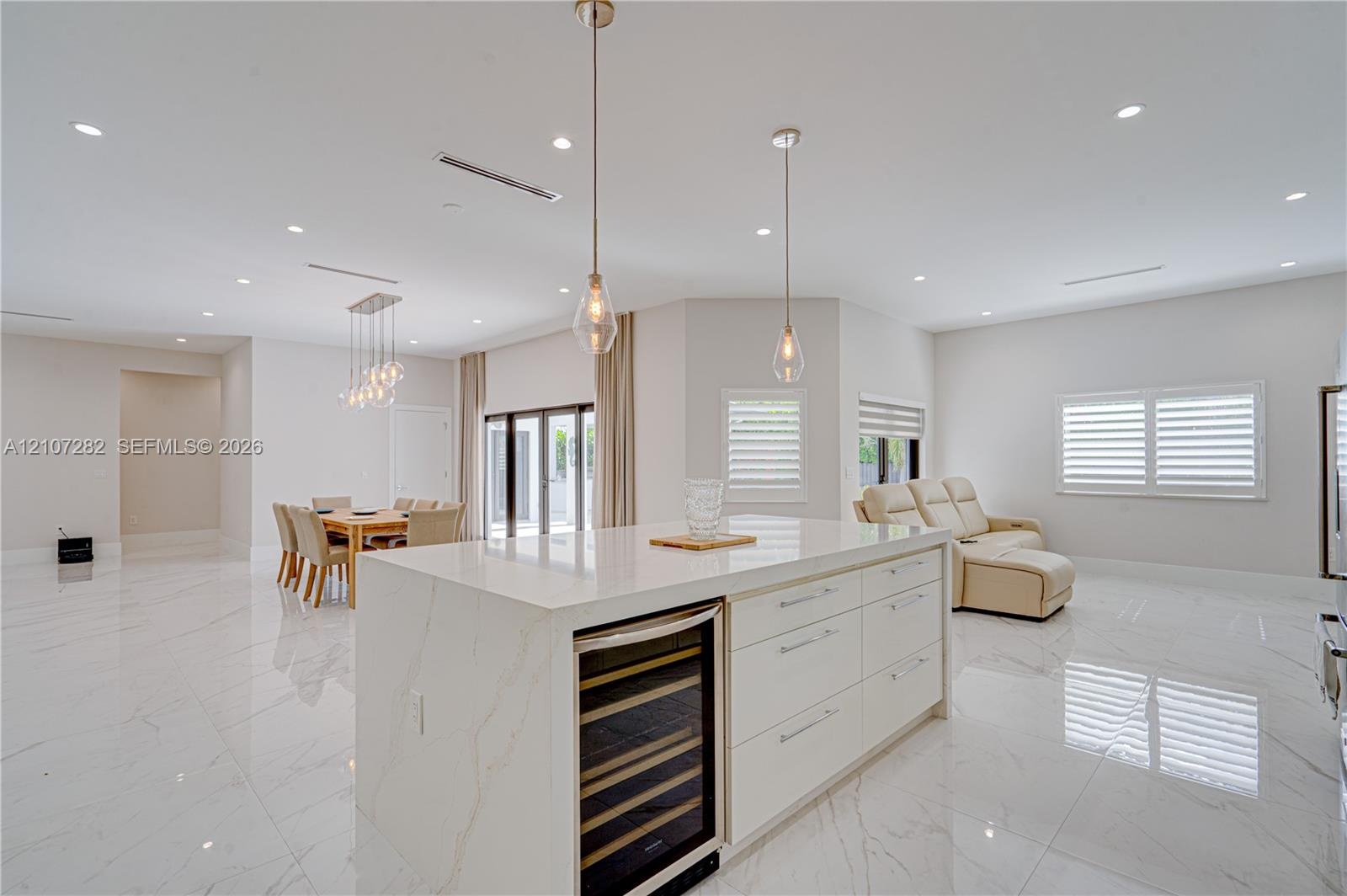 Kitchen featuring a central island with a stone-finish countertop and integrated beverage refrigerator, large-format tile flooring, recessed ceiling l