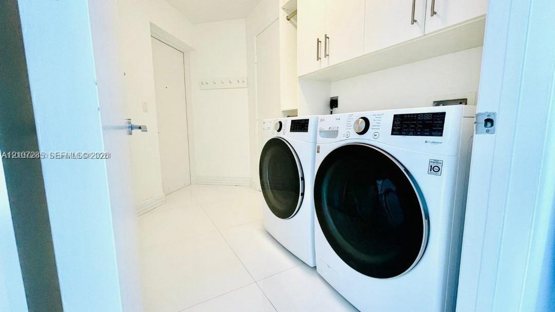 Laundry area featuring white large-format tile flooring, built-in upper cabinetry with brushed metal hardware, and a side-by-side front-loading washer