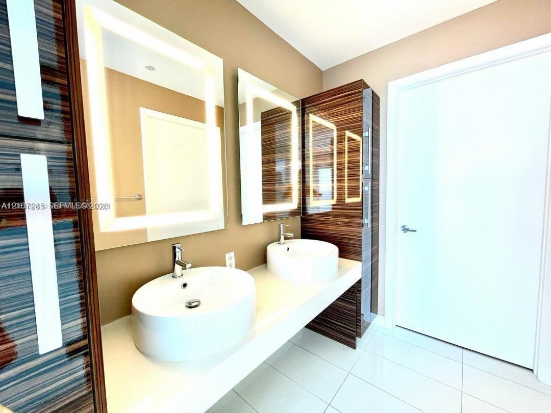 Floating double vanity featuring rectangular vessel sinks, quartz countertop, integrated wood-finish cabinetry, and back-lit mirrors with chrome fauce