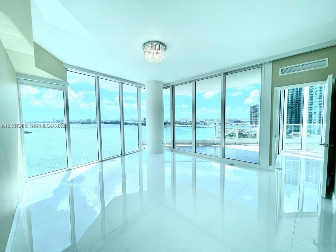 Floor-to-ceiling glass walls, polished white tile flooring, wraparound balcony, and crystal flush-mount ceiling fixture