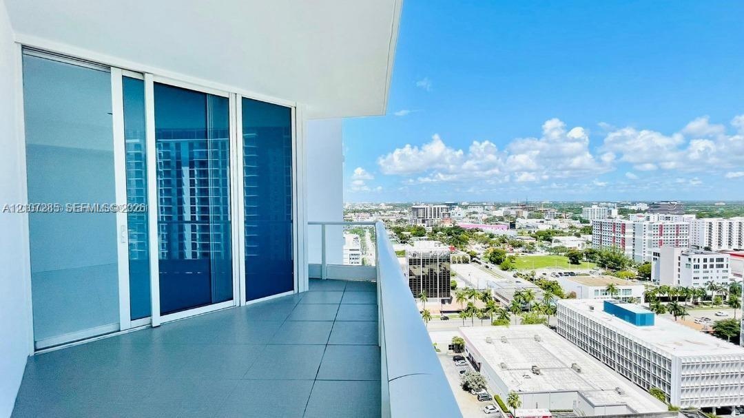 Covered balcony featuring large-format tile flooring and a glass-paneled railing, accessible through expansive floor-to-ceiling sliding glass doors