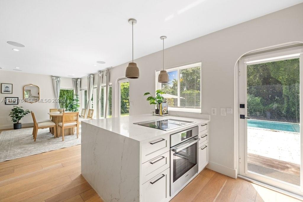 Kitchen island featuring a stone-look countertop, integrated cooktop, built-in oven, and white cabinetry, complemented by wood-finish flooring and pen