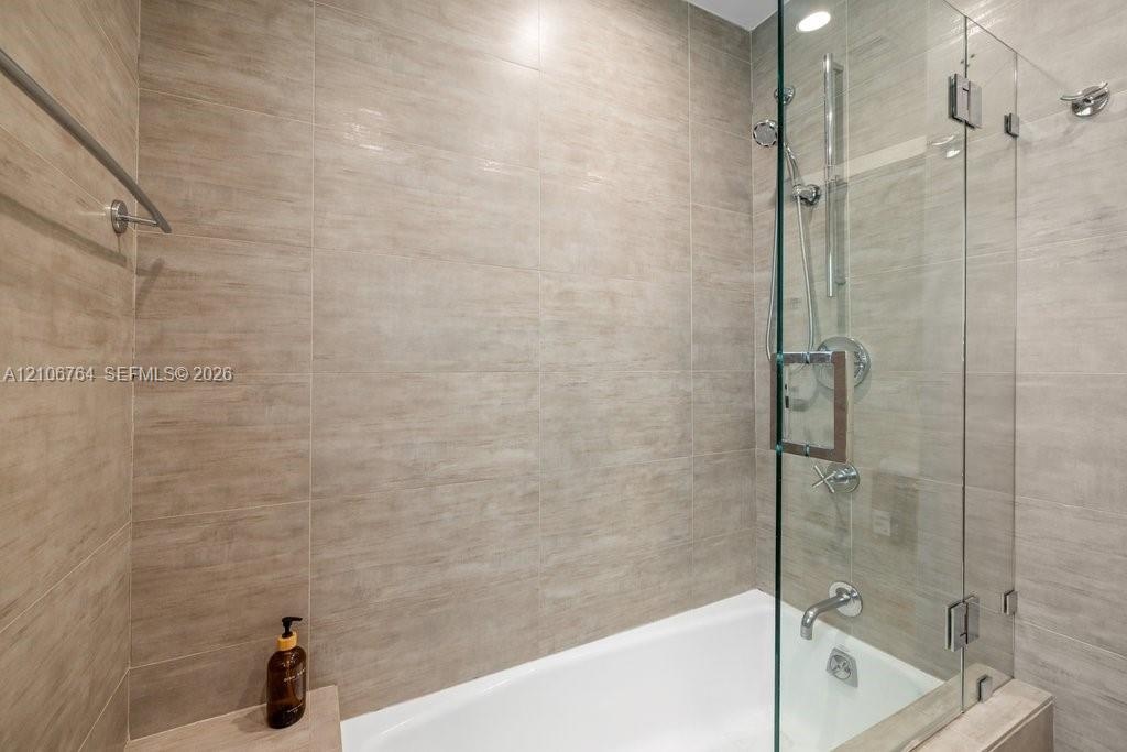 Full-height neutral-toned tile surround, frameless glass shower panel, chrome rainfall shower head with handheld attachment, built-in tub deck, and wa