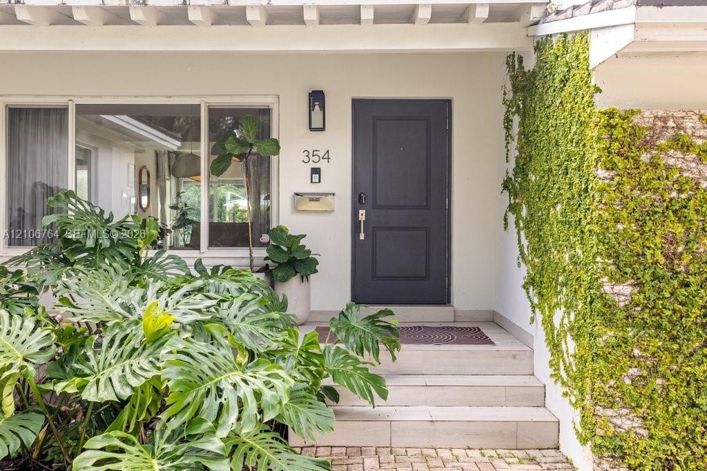 Entryway featuring a charcoal-painted front door, tiled steps, large picture window, wall-mounted metallic mailbox, and vine-covered stone siding