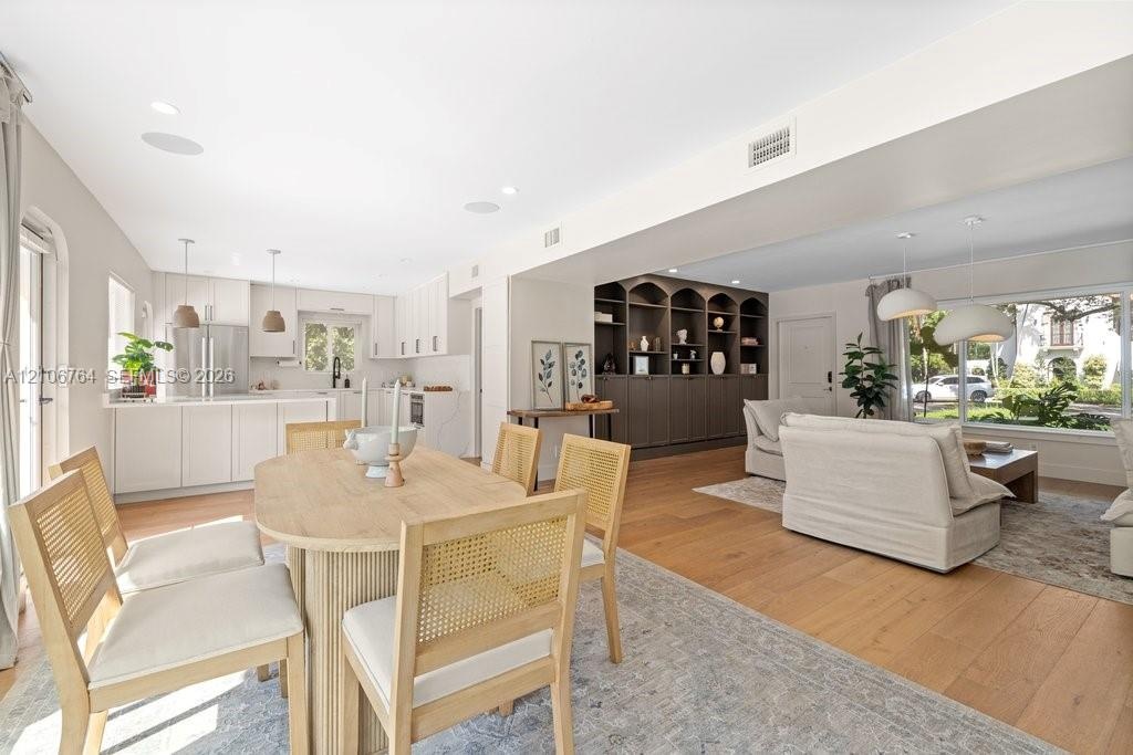 Open-concept kitchen and dining area featuring white shaker-style cabinetry, wood-finish flooring, custom built-in arched shelving, and recessed light