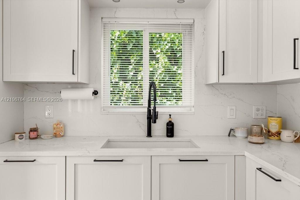White shaker-style cabinetry with matte black hardware, stone-patterned countertops, integrated white apron-front sink, matte black gooseneck faucet, 