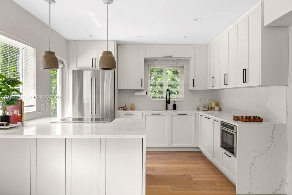 Kitchen featuring white cabinetry with matte black hardware, stone countertops with matching backsplash, wood-finish flooring, stainless steel built-i