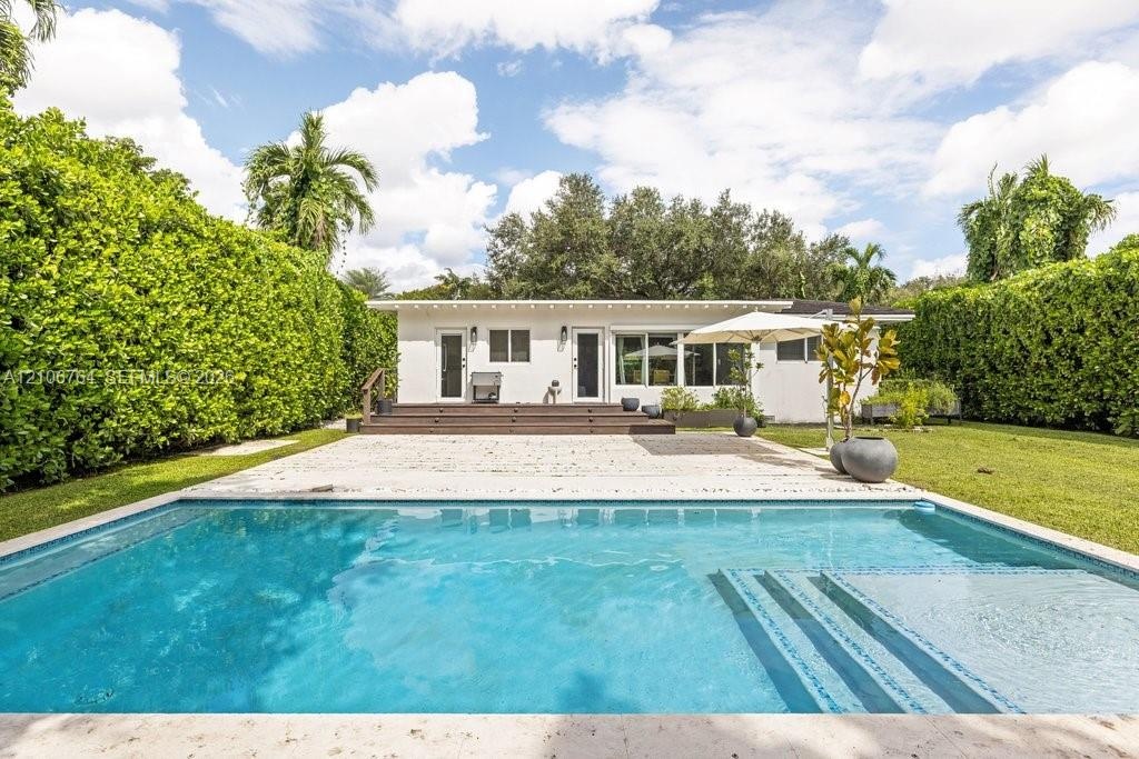 Outdoor area featuring a swimming pool with integrated steps, stone-finish pool deck, elevated wood-finish deck, and surrounding manicured privacy hed