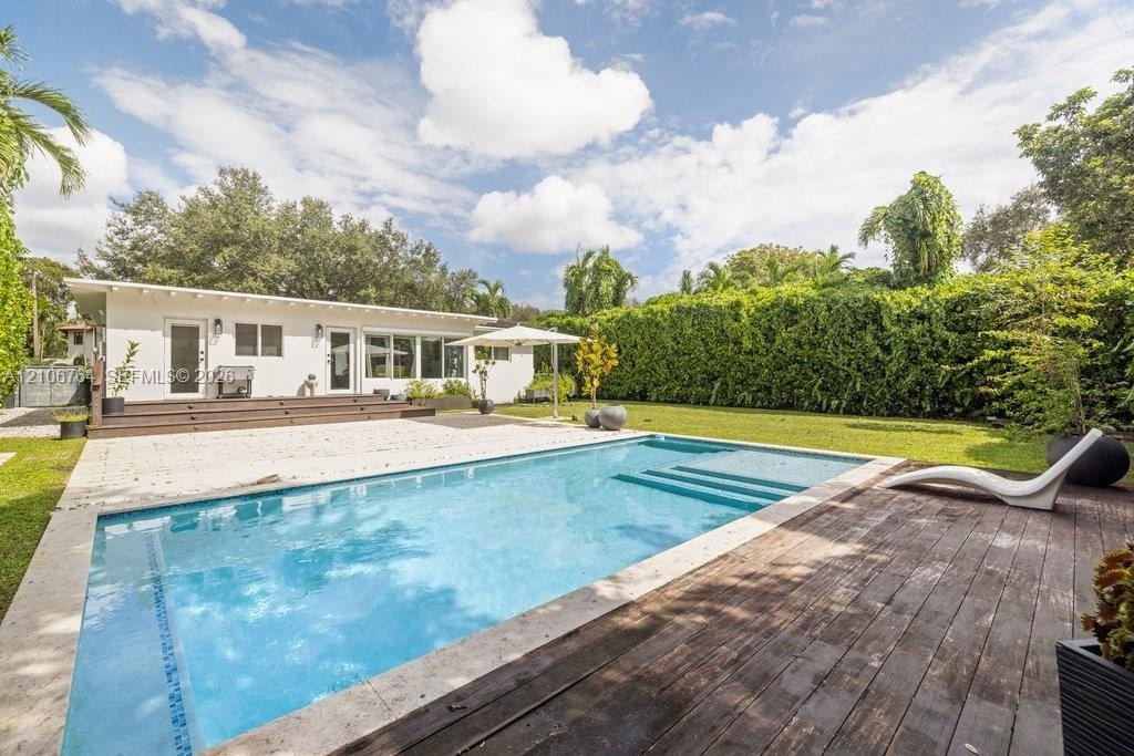 In-ground swimming pool featuring a tanning ledge, travertine pool deck, wood-finish decking, and extensive mature landscaping