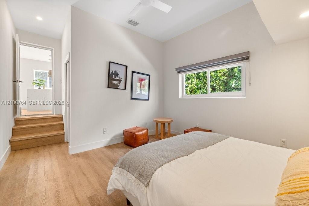 Room featuring wood-finish flooring, recessed lighting, a ceiling fan, and tiered stairs leading to a doorway