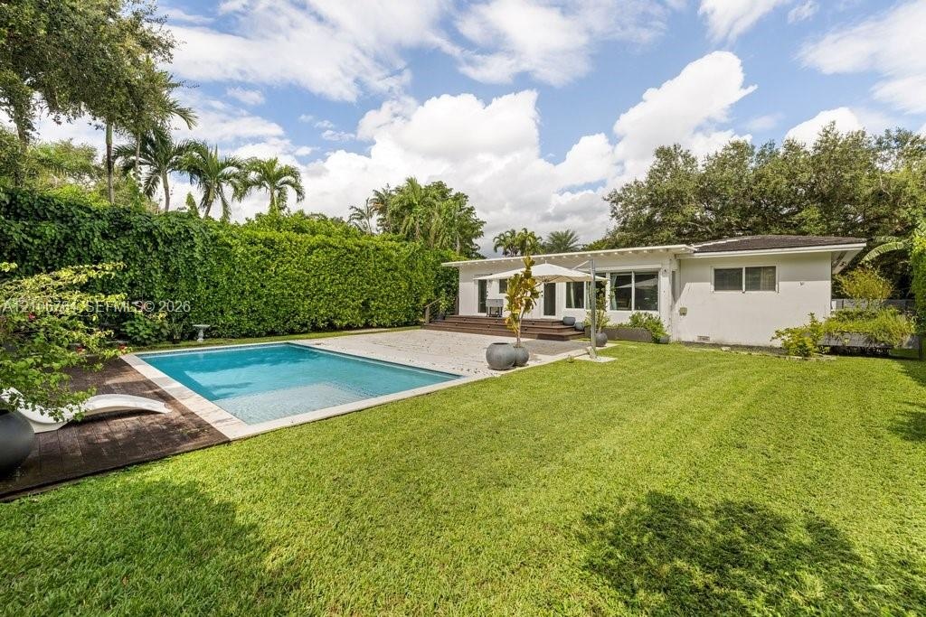 Outdoor space featuring a swimming pool, wood-finish decking, expansive lawn, and tall privacy hedging