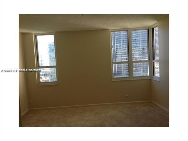 Interior space featuring neutral-toned walls, carpeting, and multiple large windows with exterior urban scenery