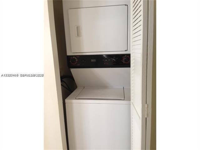 Stacked laundry center featuring a white top-load washer and front-load dryer enclosed by louvered bi-fold doors