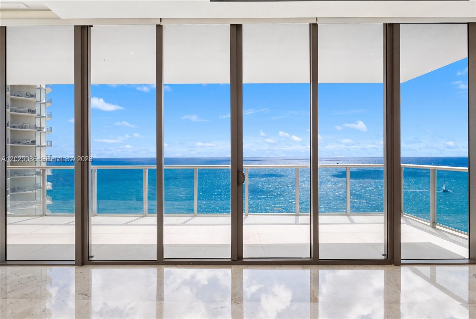 Floor-to-ceiling multi-panel sliding glass doors, private balcony with metal railing, and light-toned stone tile flooring
