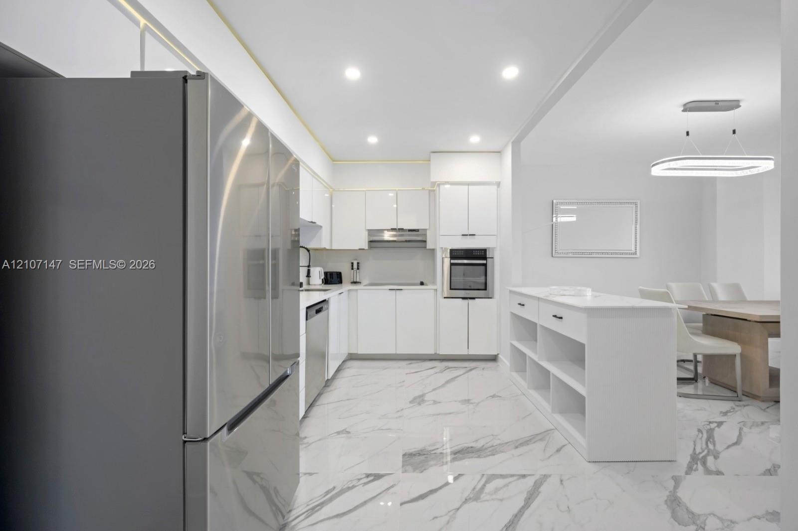 Kitchen featuring white high-gloss cabinetry, stainless steel appliances, built-in island with open shelving, recessed lighting, and large-format tile