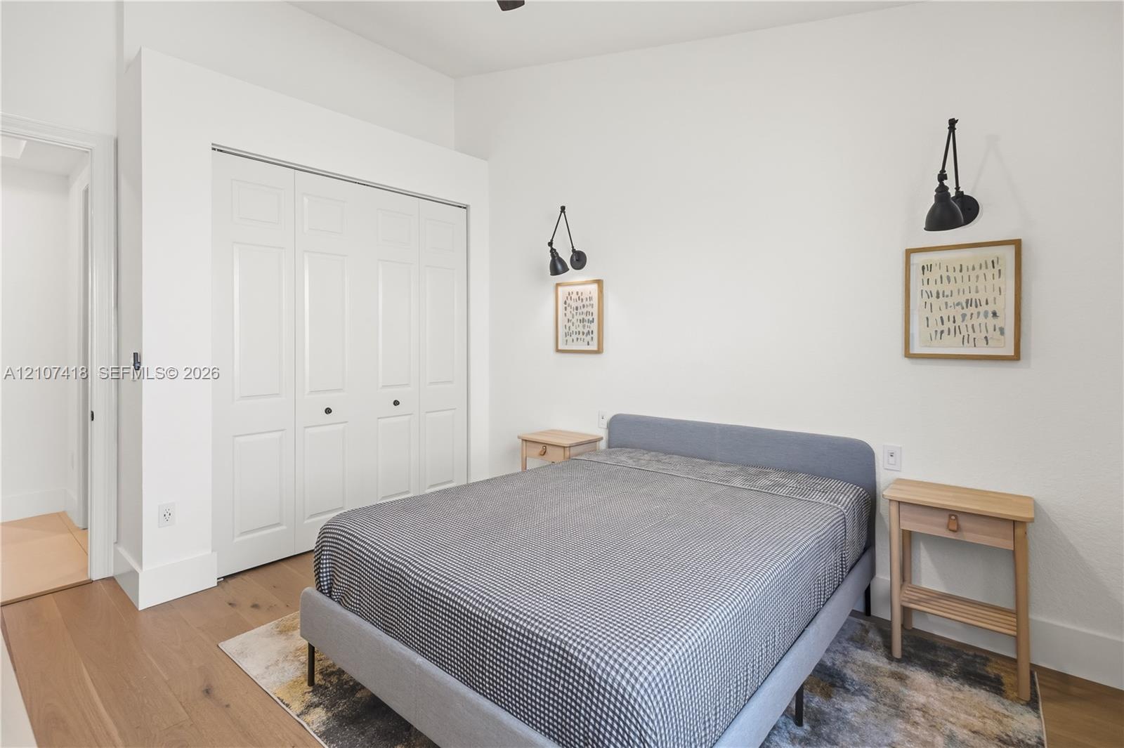 Room featuring wood-finish flooring, white bi-fold closet doors, and dual black wall-mounted swing-arm sconces