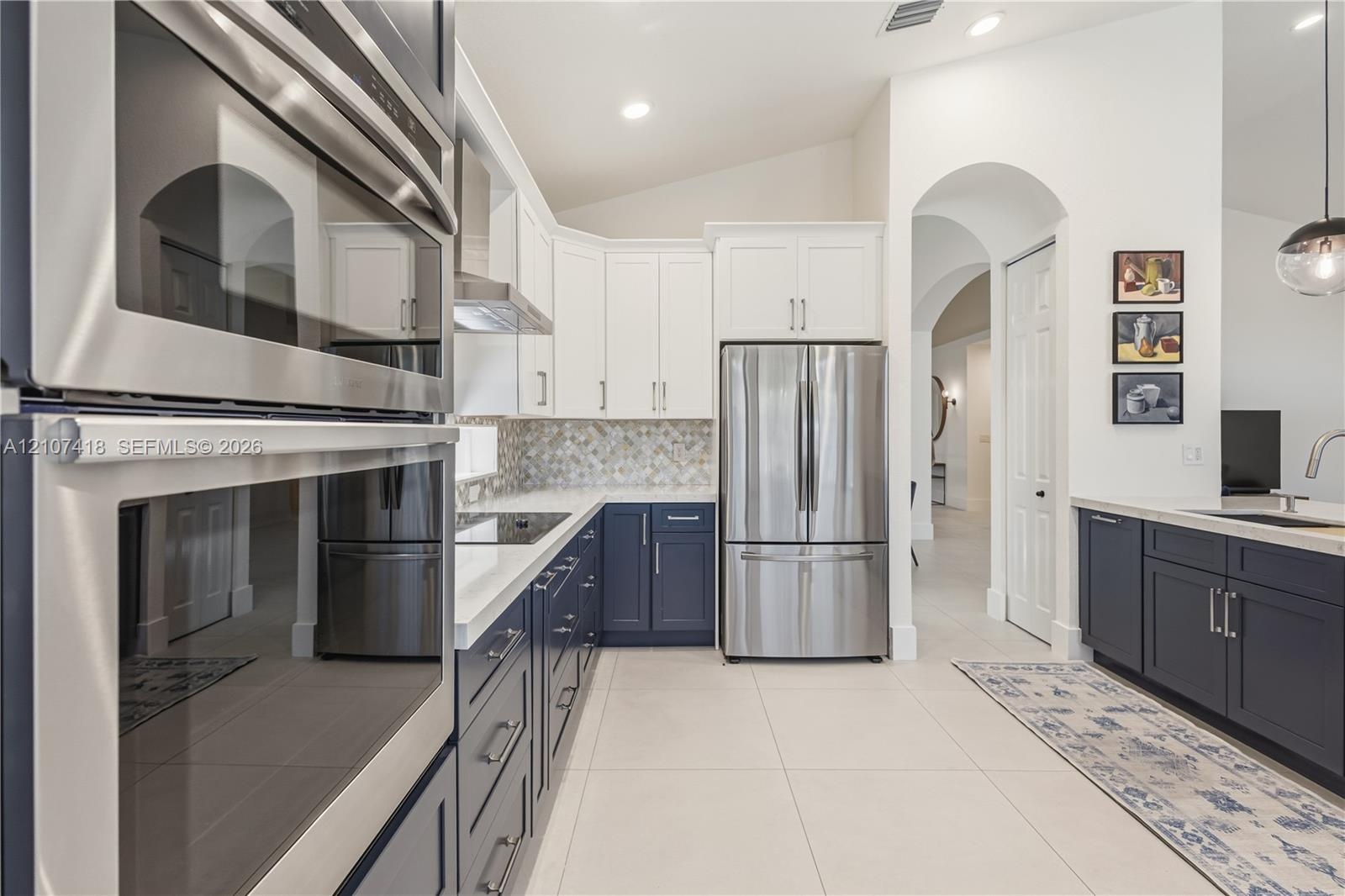Kitchen featuring dual-tone cabinetry, stainless steel appliances, quartz countertops, mosaic tile backsplash, and large-format tile flooring