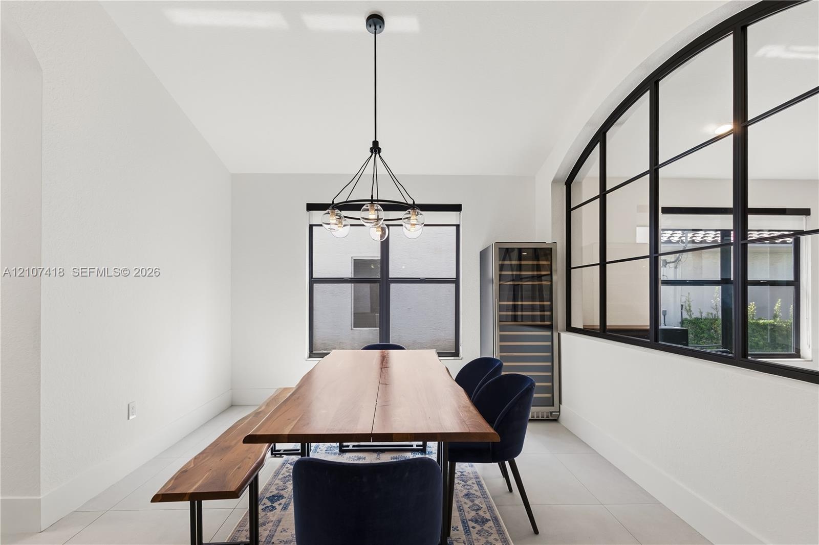 Black metal-framed glass partition, modern multi-globe chandelier, built-in wine refrigerator, and tile flooring