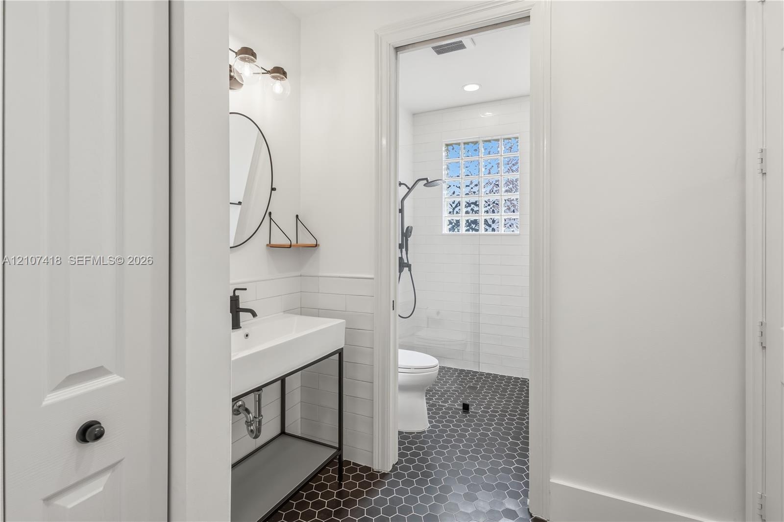 Bathroom featuring a console-style vanity with a rectangular sink, matte black plumbing fixtures, white subway tile wall treatments, and hexagonal flo