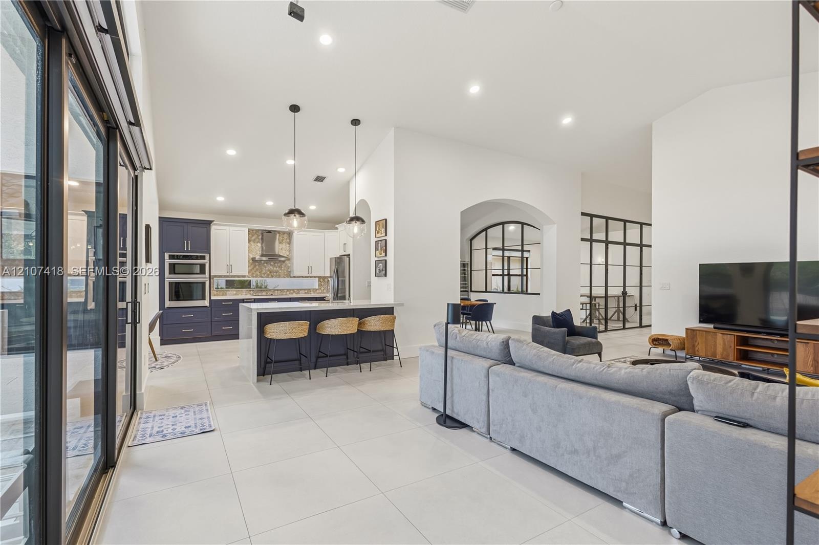 Open-concept kitchen featuring two-toned cabinetry, a large central island, recessed lighting, glass-paneled interior partitions, and porcelain tile f