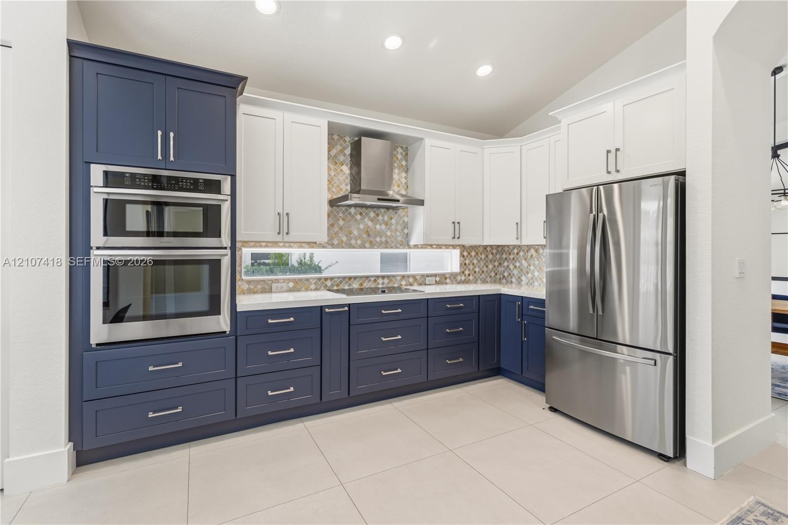 Kitchen featuring two-tone cabinetry, stainless steel double wall oven, stainless steel refrigerator, patterned mosaic tile backsplash, and quartz cou