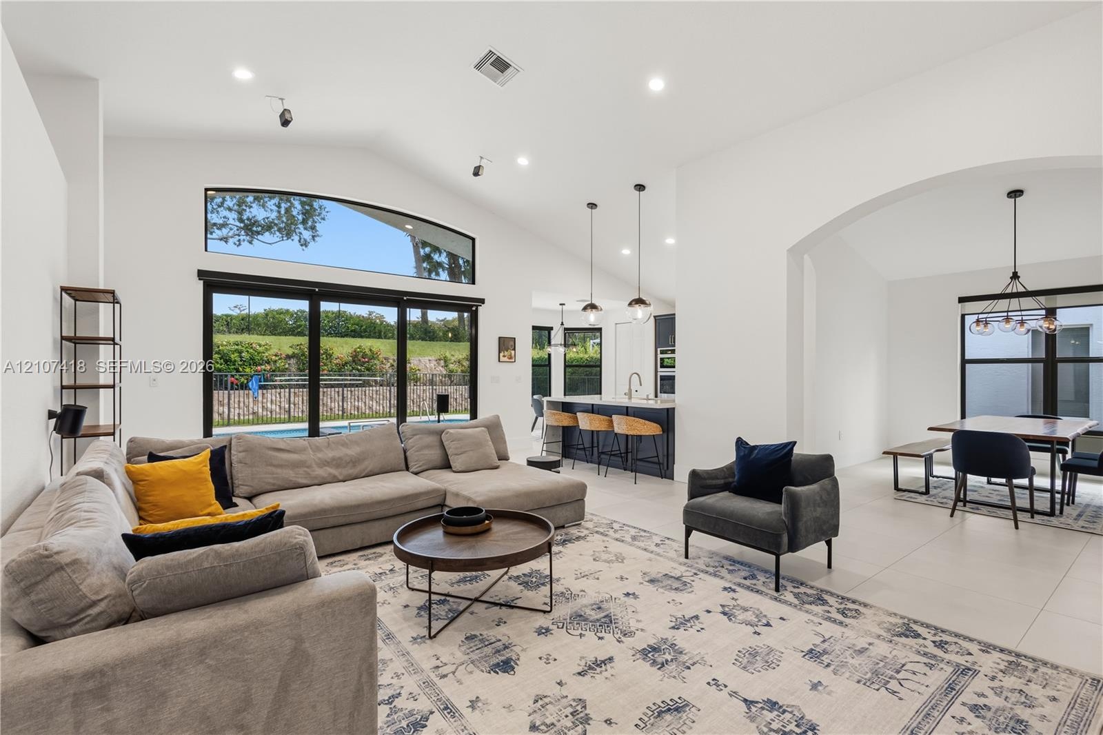 Vaulted ceilings, expansive windows with exterior transom, large-format tile flooring, recessed lighting, and kitchen island with pendant fixtures