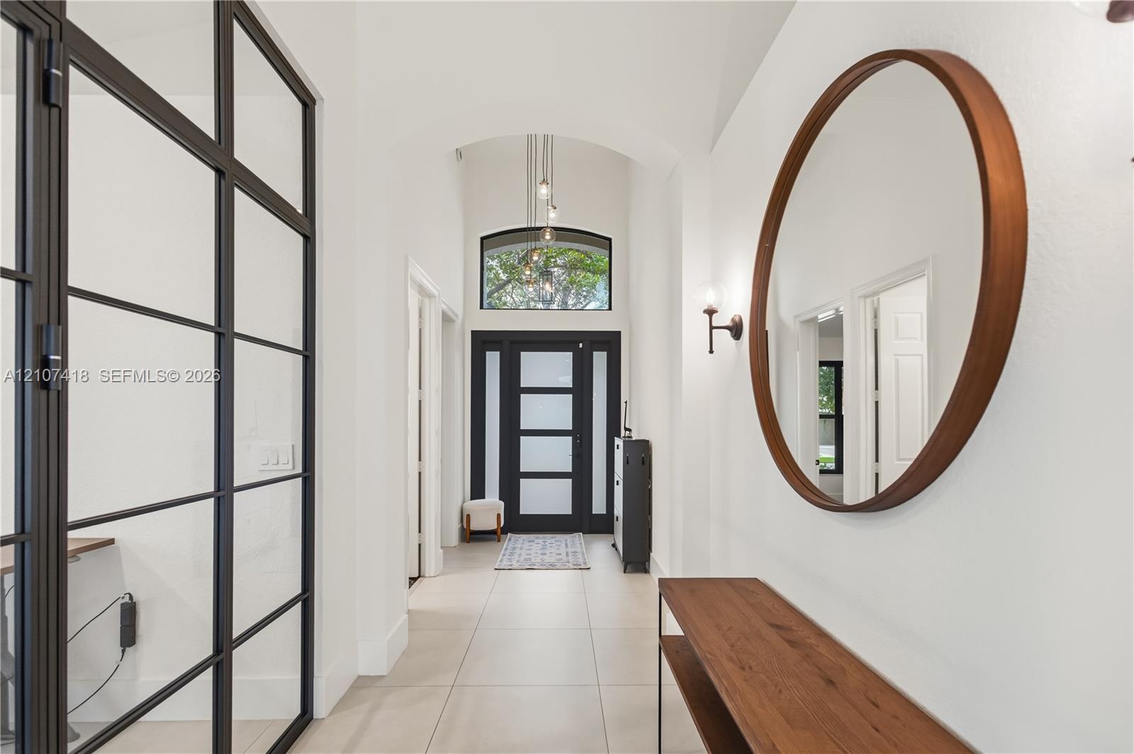 Entryway featuring large-format tile flooring, a vaulted ceiling with a pendant light, an arched transom window, and a metal-framed glass partition wa
