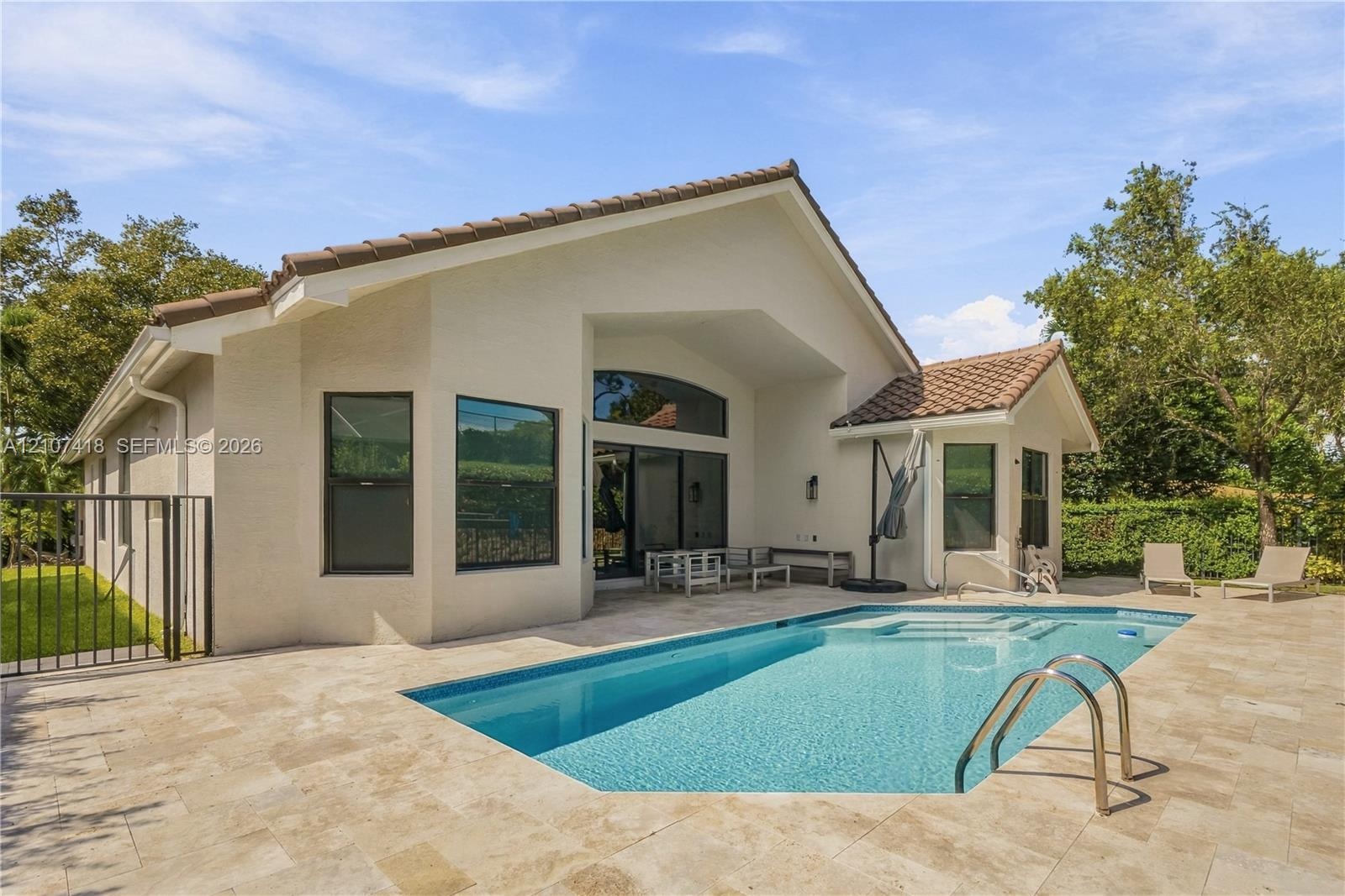 Rear exterior featuring a tile roof, stucco siding, stone paver decking, and a built-in swimming pool