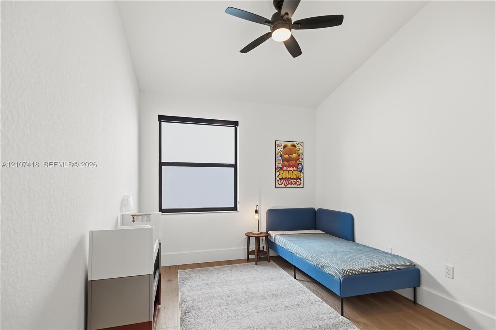Room featuring wood-finish flooring, a matte black multi-blade ceiling fan with integrated lighting, and a window with a matte black frame
