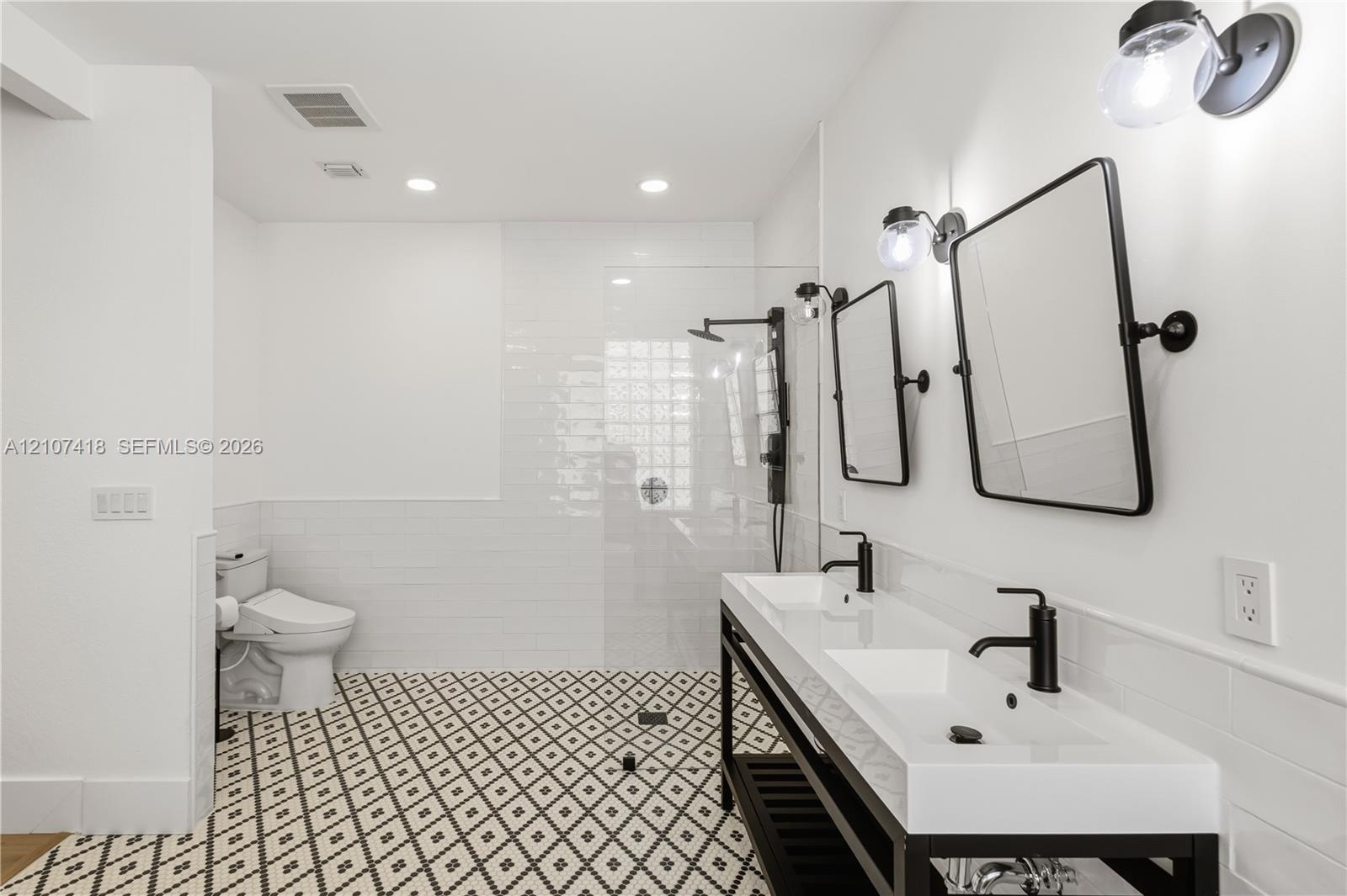 Dual vanity with rectangular sinks, matte black fixtures, framed mirrors, glass-enclosed shower, and geometric patterned tile flooring